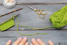 someone is knitting yarn on the table with scissors and other crafting supplies around them