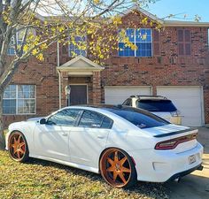 a white sports car parked in front of a brick house with orange wheels and rims