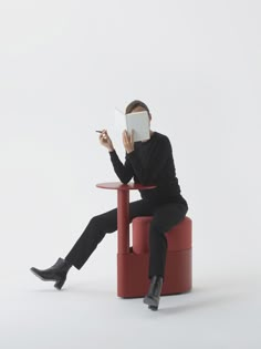 a woman sitting on a red chair reading a book with her head covered by a mask