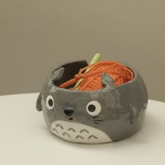 a gray and white cat shaped container with yarn in it's mouth, sitting on top of a table