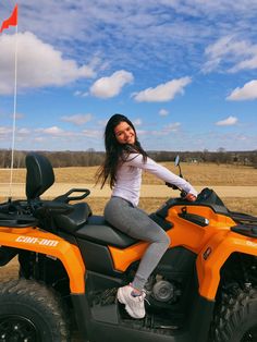 a woman sitting on top of an orange four - wheeler in front of a field