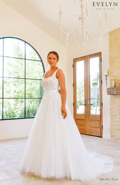 a woman in a white wedding dress standing by a window with a chandelier