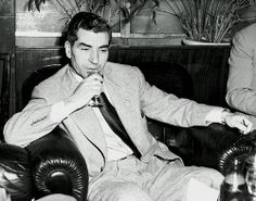 black and white photograph of two men in suits sitting on couches, one with his mouth open