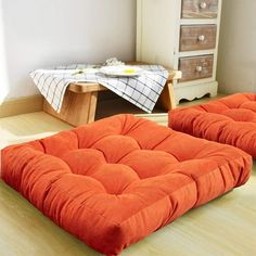 two orange futons sitting on the floor in front of a dresser and table