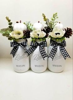 three mason jars with flowers and pine cones in them