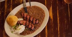 a white plate topped with meat and beans covered in gravy next to bread