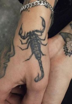 two people with tattoos on their hands holding each other's hand and one has a scorpion tattooed on it