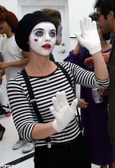 a woman with white makeup and face paint holding her hands up in the air while standing next to other people