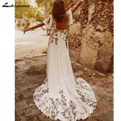 a woman in a white dress is standing near a stone wall with her arms outstretched