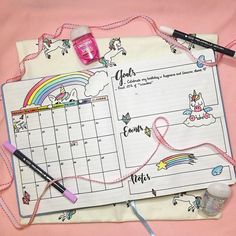 an open planner with unicorns and rainbows on it, next to some crayons