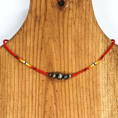 Red beaded necklace with center silver beads of varying sizes. On each side of the silver, center beads there is a segment the has black center bead with white, yellow, orange, red, and maroon beads folowing on each side. This necklace is pictured on a wooden necklace holder on a white background. Bead Loom Designs, Giddy Up Glamour, Bead Sewing, Beaded Choker Necklace, Loom Beading, Beaded Choker, Matching Earrings, Silver Beads, Seed Beads