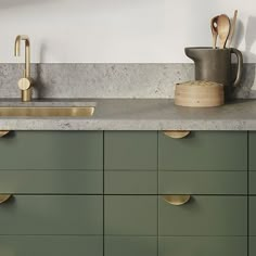 a kitchen with green cabinets and gold handles on the countertop, along with wooden utensils