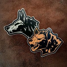 two stickers depicting the head of a wolf on a brown background with black and orange accents