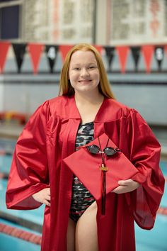 a woman in a red graduation gown standing next to a swimming pool