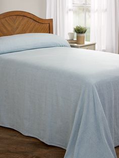 a bed with a blue bedspread and wooden headboard in front of a window