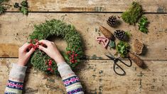 a person is decorating a wreath with berries and pine cones on a wooden table