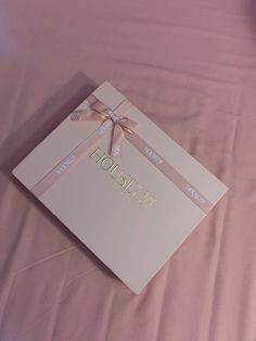 a box with a bow on it sitting on a pink sheeted tablecloth covered bed