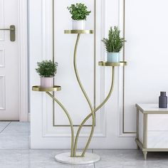 three potted plants sitting on top of two gold stands in front of a white door