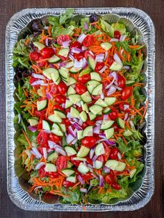 a salad with cucumbers, tomatoes, carrots and lettuce in a tin pan