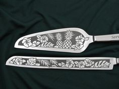 two serving utensils with pineapples and flowers on them, sitting on a green cloth