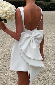 the back of a woman in a white dress holding flowers