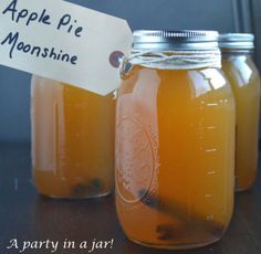 three jars filled with liquid sitting on top of a table next to a sign that says apple pie moonsshin