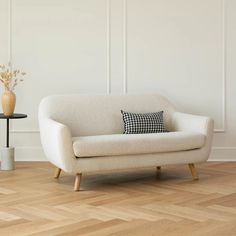 a white couch sitting on top of a hard wood floor next to a vase with flowers