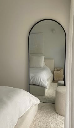 a white bed sitting under a mirror in a bedroom