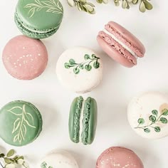 macaroons and doughnuts are arranged on a white surface with greenery