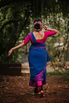 a woman in a blue and pink dress is walking through the woods with her hand on her head