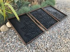 three decorative black trays sitting on top of gravel next to plants and rocks with grass in the background