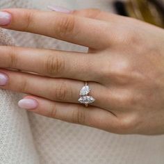 a woman's hand wearing a ring with two pear shaped diamonds on top of it