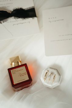 a bottle of perfume sitting on top of a bed next to an earring ring