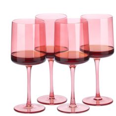 four pink wine glasses are lined up on a white surface, with one empty glass in the middle