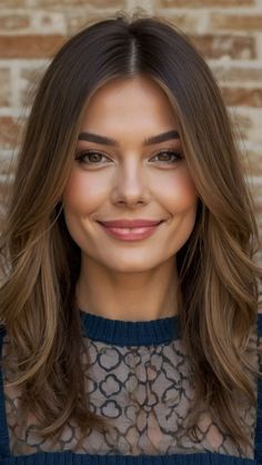 a woman with long brown hair smiling and wearing a blue top in front of a brick wall