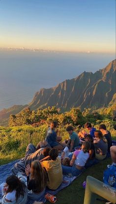 a group of people sitting on top of a lush green hillside next to the ocean