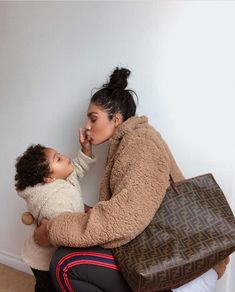 a woman sitting on the floor with a child in her lap and a handbag next to her