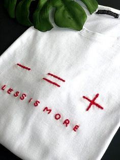 a white t - shirt with the word jesusmore embroidered on it next to a green plant