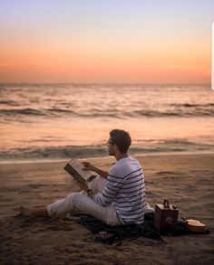 a man sitting on top of a beach next to the ocean while reading a book