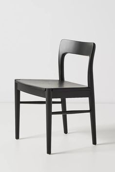 a black wooden chair sitting on top of a white floor next to an empty wall