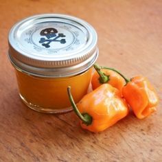 two orange peppers sitting on top of a wooden table next to a jar of jam