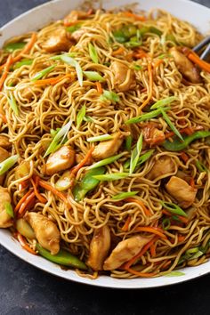 a white bowl filled with noodles and chicken on top of a table next to chopsticks