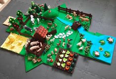 a table topped with lots of toy animals and farm scenes on top of green mats