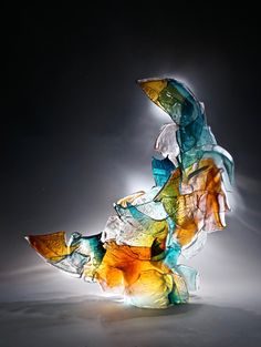 a glass sculpture sitting on top of a white table next to a black wall with light coming through it