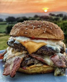 a cheeseburger on a bun with bacon and lettuce in the background