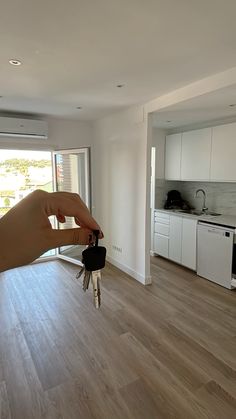 a hand is holding keys in front of an open kitchen and living room area with sliding glass doors