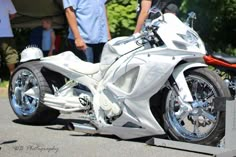 a white motorcycle parked on top of a parking lot next to other people and trees