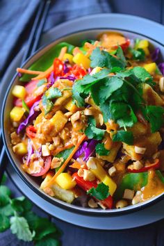 a bowl filled with colorful vegetables and garnished with cilantro, carrots, green leaves