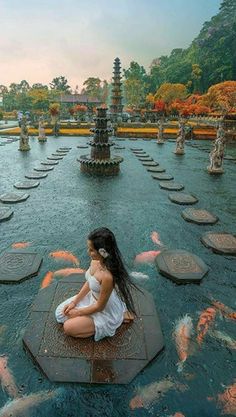 a woman sitting in front of a pond filled with fish