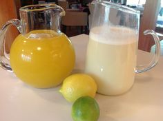 a pitcher of milk and two lemons sit on a table next to each other